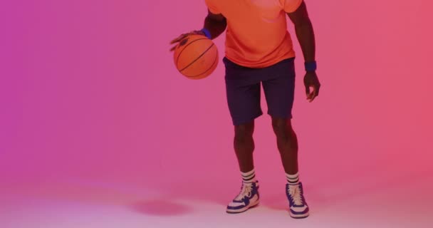 ピンクのボールをオレンジの背景に跳ねるアフリカ系アメリカ人男性バスケットボール選手のビデオ スポーツ 競技の概念 — ストック動画
