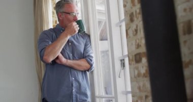 Gözlüklü, camdan bakıp kahve içen mutlu bir beyaz adam. Evde yalnız vakit geçirmek..