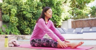 Çift ırklı kadın bahçede yoga ve esneme pratiği yapıyor.