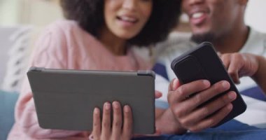 Mutlu Afro-Amerikan çift oturma odasında tablet ve akıllı telefon kullanıyor. Evde birlikte vakit geçirmek kavramı..