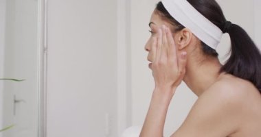 Çift ırklı bir kadın banyoda yüzüne krem sürüyor. Güzellik, sağlık ve kadın spa konsepti.