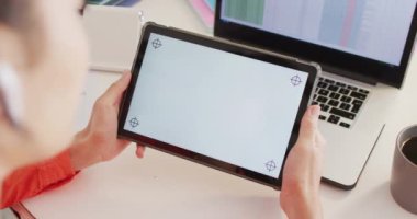 Çift ırklı kadın masada oturuyor ve fotokopi aletiyle tabletle çalışıyor.