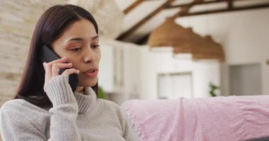 Çift ırklı kadın oturma odasında oturmuş akıllı telefonla konuşuyor.