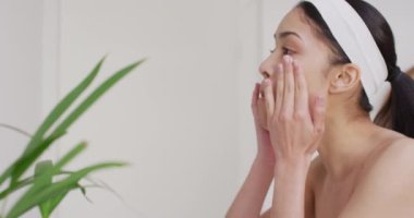 Çift ırklı bir kadın banyoda yüzüne krem sürüyor. Güzellik, sağlık ve kadın spa konsepti.