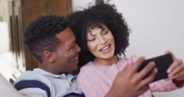 Mutlu Afro-Amerikan çift oturma odasında akıllı telefon kullanıyor. Evde birlikte vakit geçirmek kavramı..
