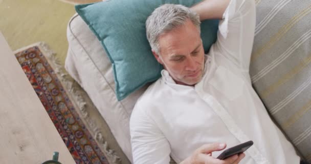 ชายผ วขาวท ความส ขนอนบนโซฟาในห องน งเล นใช สมาร ทโฟน เวลาอย — วีดีโอสต็อก