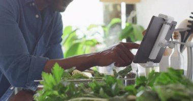 Afro-Amerikalı adam, tablet kullanarak mutfakta yemek pişiriyor. Evde yalnız zaman geçirmek..