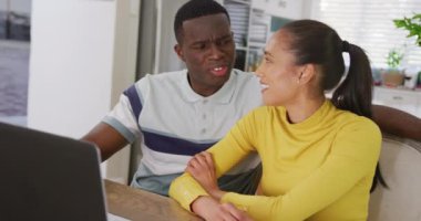 Mutfakta oturup dizüstü bilgisayar izleyen ve gülümseyen mutlu çiftin videosu. İletişim, mutluluk, aşk, ev hayatı ve kapsayıcılık kavramı.