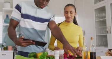 Mutfakta birlikte yemek hazırlayan mutlu çiftin tablet tarifini kullandıkları bir video. İletişim, mutluluk, sağlık, ev hayatı ve kapsayıcılık kavramı.