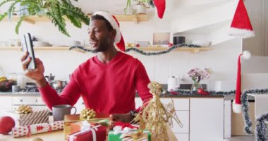 Mutlu Afro-Amerikan adam Noel Baba şapkası takıyor, video görüşmesi için akıllı telefonu kullanıyor. Noel 'de evde yalnız vakit geçirmek..