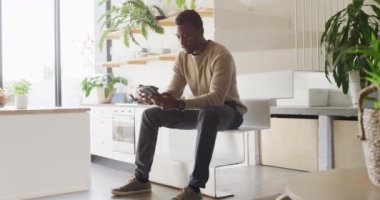 Mutlu Afro-Amerikan adam merdivenlerde oturuyor, kahve içiyor ve akıllı telefon kullanıyor. Evde yalnız zaman geçirmek..