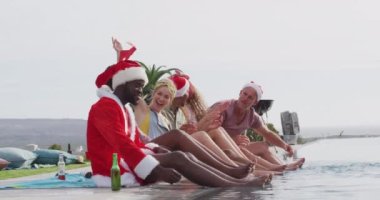 Altı farklı mutlu arkadaş Noel 'i kostümlerle, dışarıda yüzme havuzunda ayaklarıyla kutluyor. Noel, kutlama, gelenek, arkadaşlık, kapsayıcılık ve yaşam tarzı konsepti.