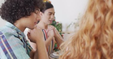 Masada oturup yemek yiyen, birlikte dua eden bir grup mutlu arkadaş. Noel 'de evde birlikte vakit geçirmek..