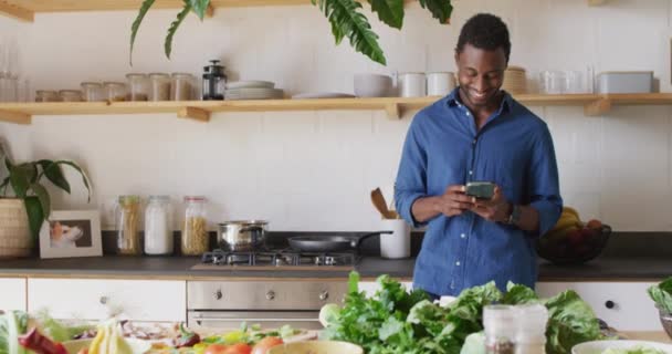 幸せなアフリカ系アメリカ人男性の台所で夕食を調理 スマートフォンを使用して 自宅だけで質の高い時間を過ごす — ストック動画