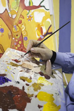 bir kutu, renk paleti ve fırça ile çalışan ressam