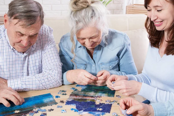 Middle-aged family elderly collects jigsaw puzzles at the table in the room