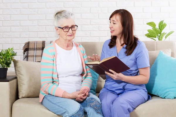 Nurse reads a book to an elderly woman domab rehabilitation and nursing home concept