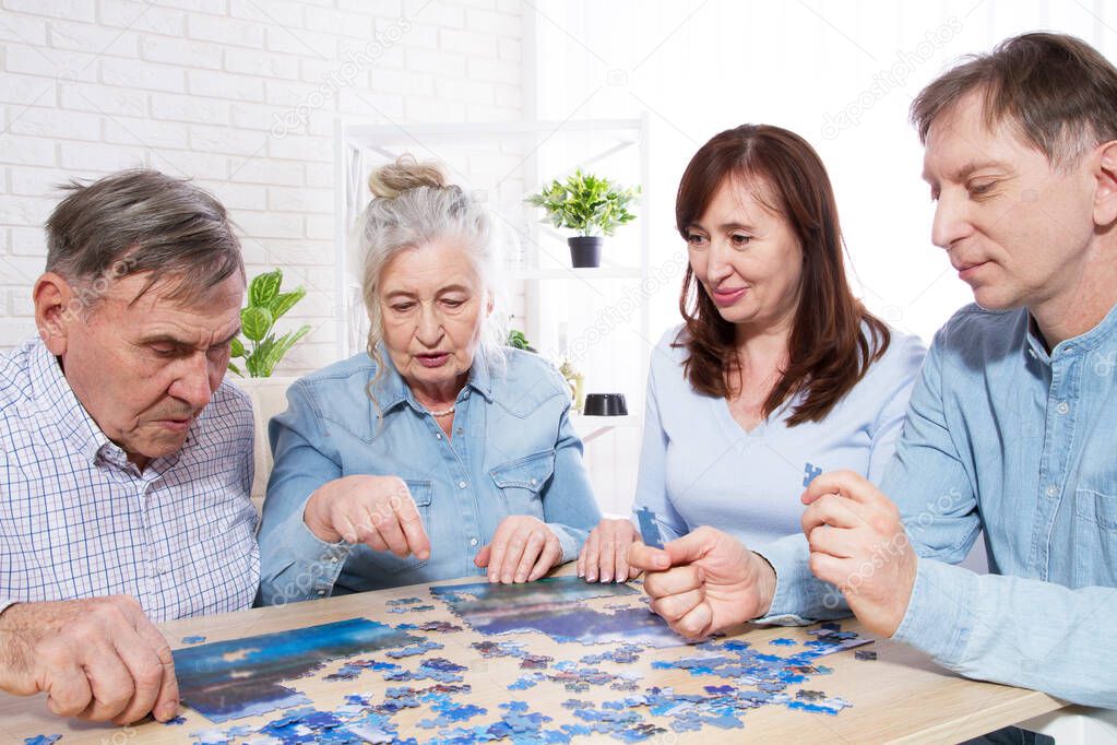 elderly couple and middle-aged couple working on a jigsaw puzzle together at home