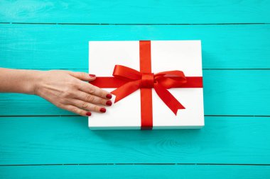 Mavi ahşap arka planda hediye kutusunda kırmızı tırnakları olan bir kadın. Üst görünüm