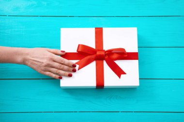 Mavi ahşap arka planda hediye kutusunda kırmızı tırnakları olan bir kadın. Üst görünüm