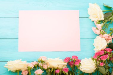 Mavi ahşap arka planda renkli güllerin çerçevesi. Kağıt kart ve kopyalama alanı da var. Üst görünüm ve seçici odaklanma. Model