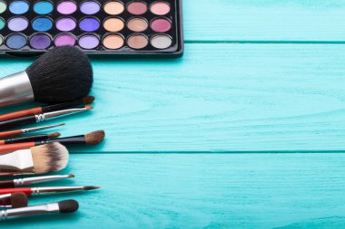 Makyaj aletleri. Makyaj ürünleri. Ruj, göz farı, brushe. Mavi ahşap arka planda kozmetik ürünleri. Seçmeli odak noktası.