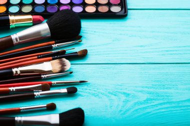 Makyaj aletleri. Makyaj ürünleri. Ruj, göz farı, brushe. Mavi ahşap arka planda kozmetik ürünleri. Seçmeli odak noktası.