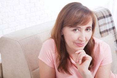 Gülümseyen bayanın makro portresi. Çekici ve güzel orta yaşlı kadın koltukta oturuyor ve evde dinleniyor. Menopoz