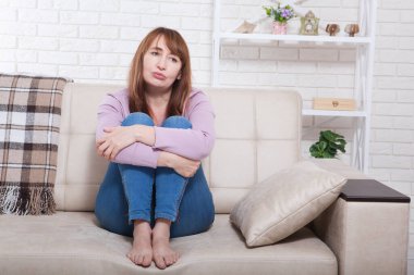 Depresyonda ve üzgün orta yaşlı bir kadın dizleri kelepçeli bir şekilde yatakta oturuyor, koç, evinde bir kanepe. Boşluğu kopyala