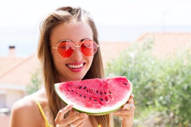 Deniz kıyısındaki otellerin arka planında karpuz olan gülümseyen kız.