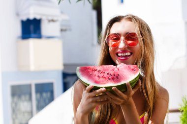 Otelde poz veren ve karpuz yiyen bir kadın.