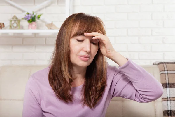 Brunette middle aged woman having headache on home background. Menopause