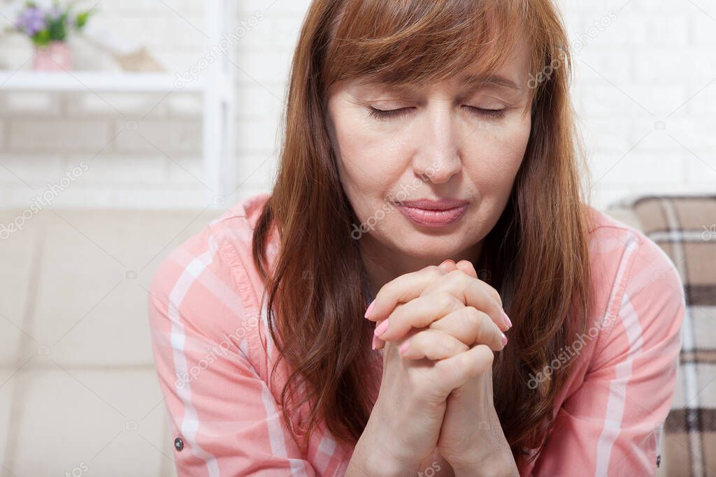 Portrait of pretty middle age woman praying and dreaming at home background. Menopause. Copy space