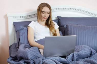 Güzel bir kadın dizüstü bilgisayarla yatakta yatıyor, tatlı bir kız sabahları dizüstü bilgisayar kullanıyor, evde serbest çalışıyor.