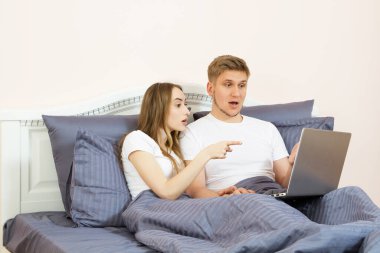 Genç, güzel bir çift yatak odasında uzanıyor ve görüntülü sohbet kullanarak dizüstü bilgisayarla konuşuyorlar.