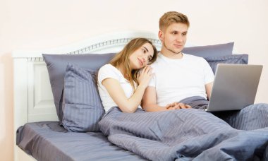 Genç ve güzel bir çift yatak odasında yatıyorlar ve dizüstü bilgisayar kullanıyorlar.