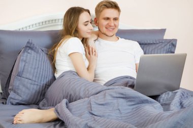 Genç ve güzel bir çift yatak odasında yatıyorlar ve dizüstü bilgisayar kullanıyorlar.