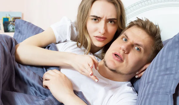 Displeased couple is lying in bed and looking at the camera, problem in relationships, angry people, bad sleep