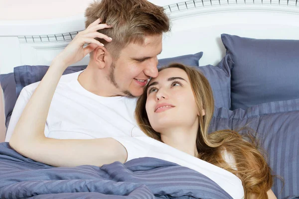 Beautiful awakened loving couple in bed in the morning. Young adult heterosexual couple lying on bed in bedroom.