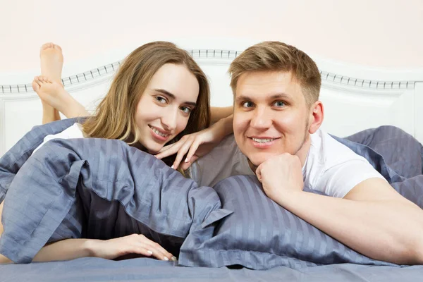 Cute loving couple is lying on the bed in the bedroom in the morning. Young happy couple lying in bed and smile