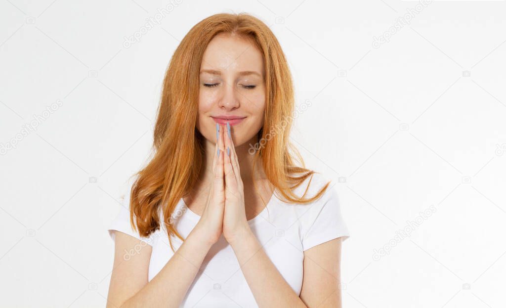 Closeup portrait of a young red head woman praying. Red hair beautiful girl isolated on white. Concentrated redhair woman in t-shirt praying with pray gesture and closed eyes.
