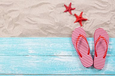 Kırmızı denizyıldızı ve parmak arası terlikler kumda ve ahşap tahta üst görünümde.