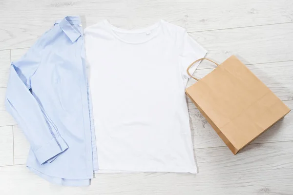 White t shirt and paper bag mock up on wooden background. Top view and copy space. Mockup t-shirt and summertime. Template blank shirt.
