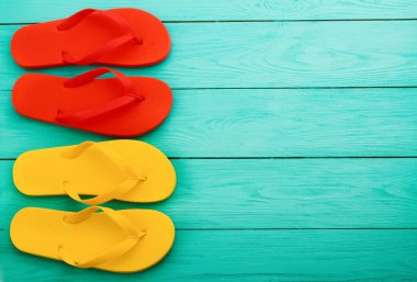 Fotokopi alanı olan mavi ahşap arka planda renkli parmak arası terlikler. Üst görünüm ve seçici odak