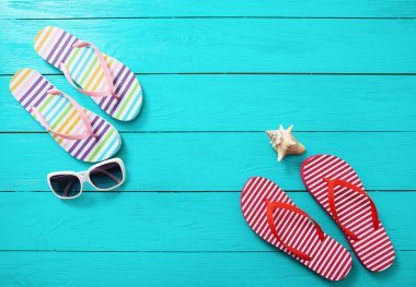 Terlikler, güneş gözlükleri ve mavi ahşap arka planda deniz kabuğu. Boşluk ve moda yaz aksesuarlarını kopyala.