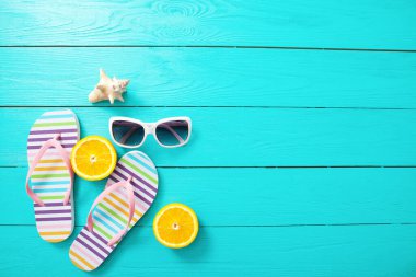 Mavi ahşap arka planda terlikler, güneş gözlükleri ve portakallar. Üst görünüm ve kopyalama alanı