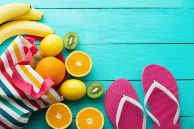 Yaz eğlencesi ve mavi ahşap arka planda meyveler. Model ve resim gibi. Portakal, limon, kivi, poşette muz meyvesi ve yerde parmak arası terlik. Üst görünüm ve kopyalama alanı