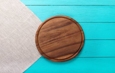 Gri keten masa örtüsü üzerinde tatil yemekleri için kahverengi yuvarlak kesim tahtası. Restoranda mavi ahşap arka plan. Üst manzara.