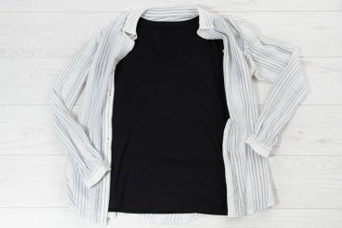 Siyah yakın plan tişört beyaz ahşap arka planda düz duruyor. Üst görünüm ve boşluk kopyala. Model tişört ve yaz tatili. Şablon boş gömlek.