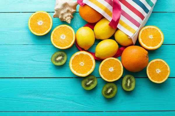 Summer fun time and fruits on blue wooden background. Mock up and picturesque. Orange, lemon, kiwi fruit in bag and shell on the table. Top view and copy space. Mock up